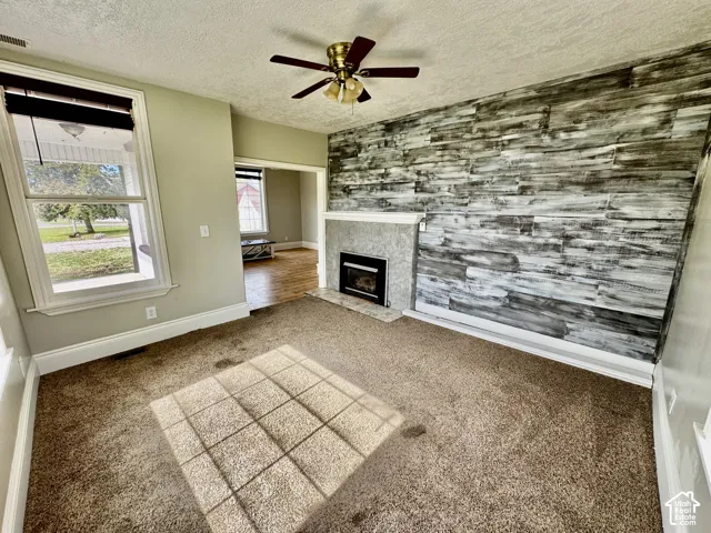 Carpeted living space featuring a ceiling fan, a fireplace with a mantel, and a decorative wood-finish accent wall