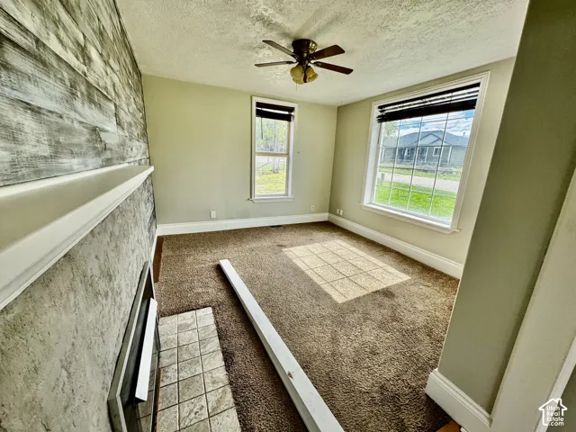 Fireplace with tile hearth, wood-style accent wall, and ceiling fan