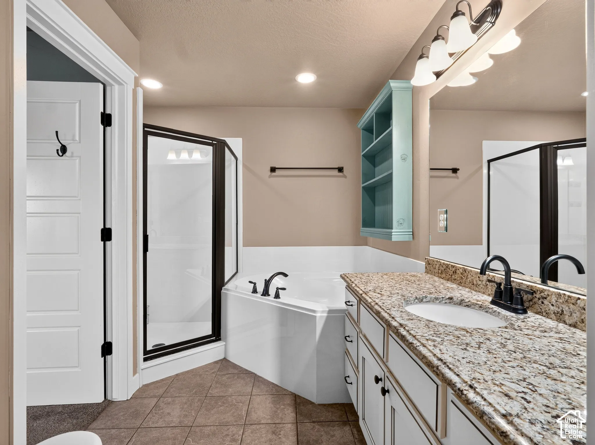 Dual-sink vanity with a light-toned countertop, a corner soaking tub, a stand-up shower with a glass enclosure, and tiled flooring