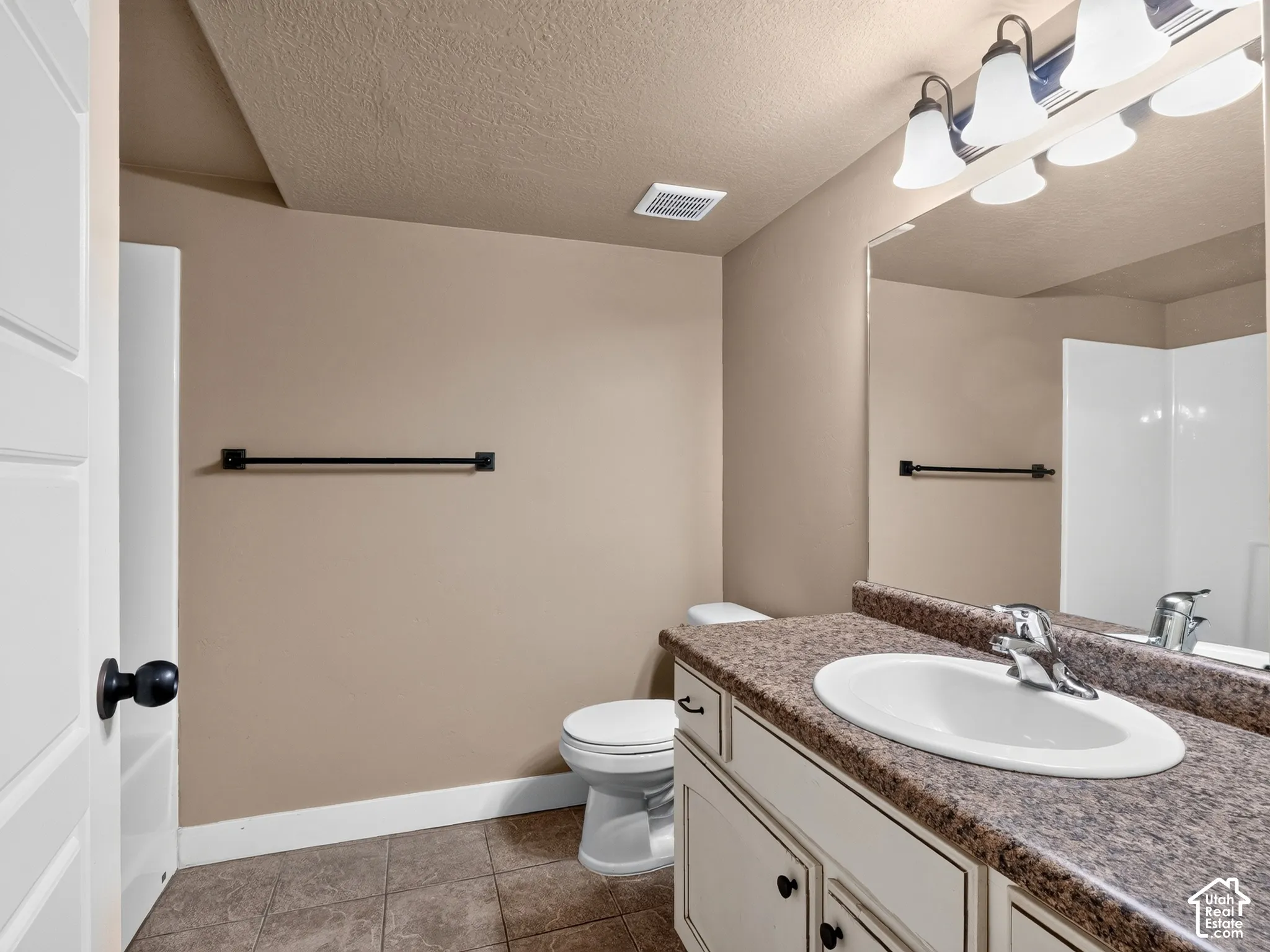 Vanity with a speckled countertop and integrated sink, white cabinetry with black hardware, large wall mirror, and tile flooring