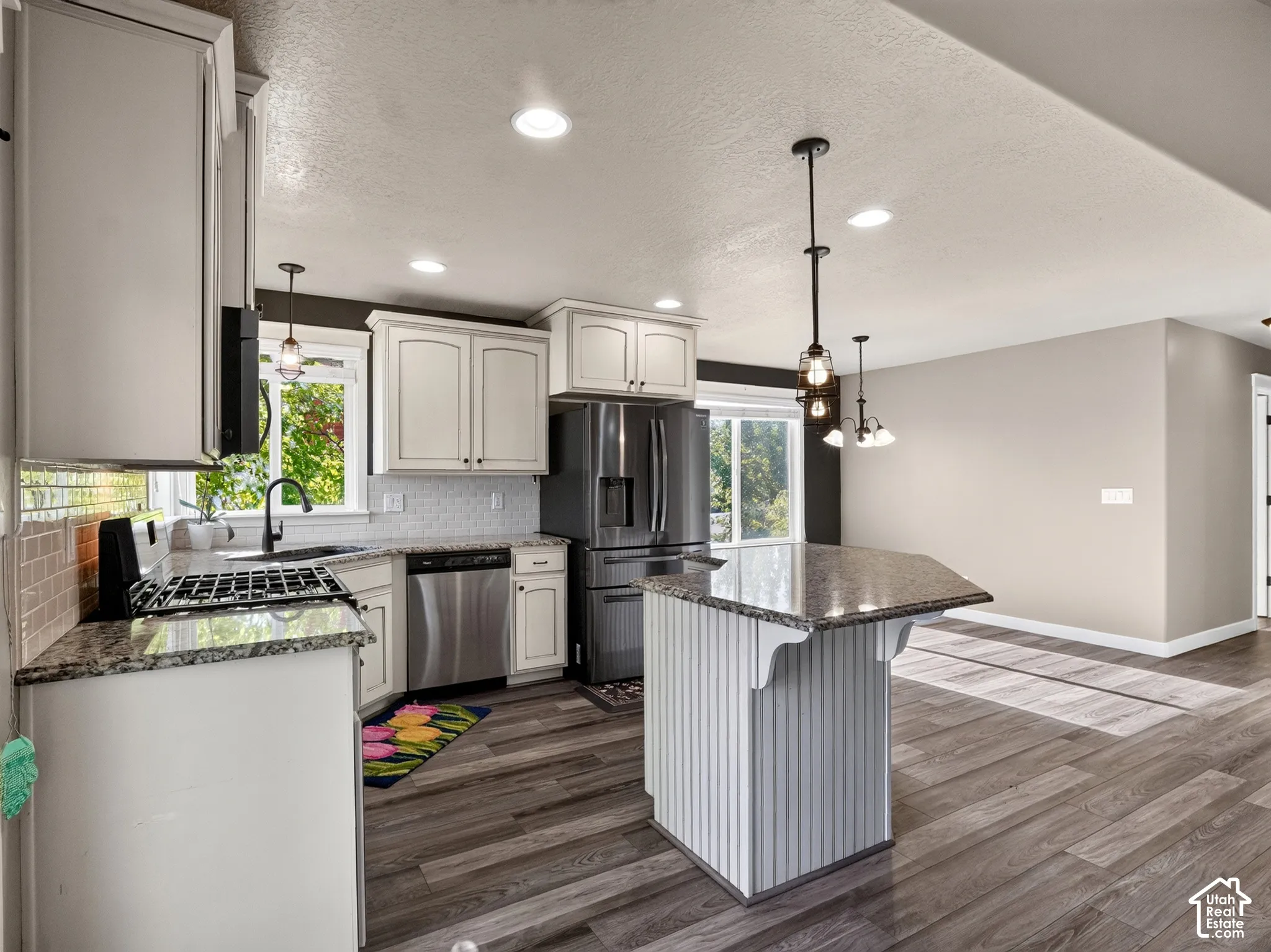 Kitchen featuring wood-finish flooring, white cabinetry, a central island with a granite-style countertop, and stainless steel appliances