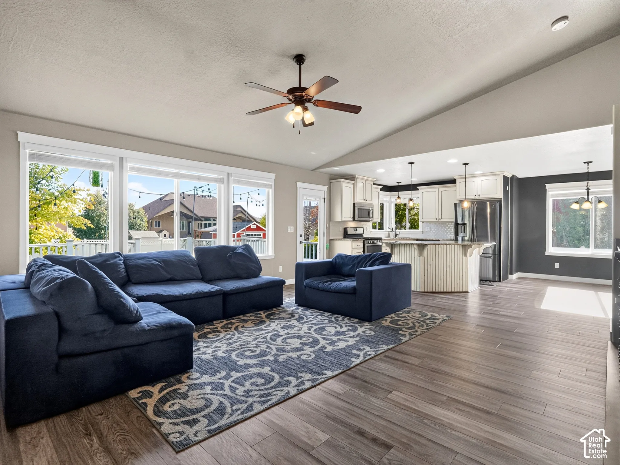 Spacious living area featuring large windows, vaulted ceiling with a fan, wood-finish flooring, and recessed lighting
