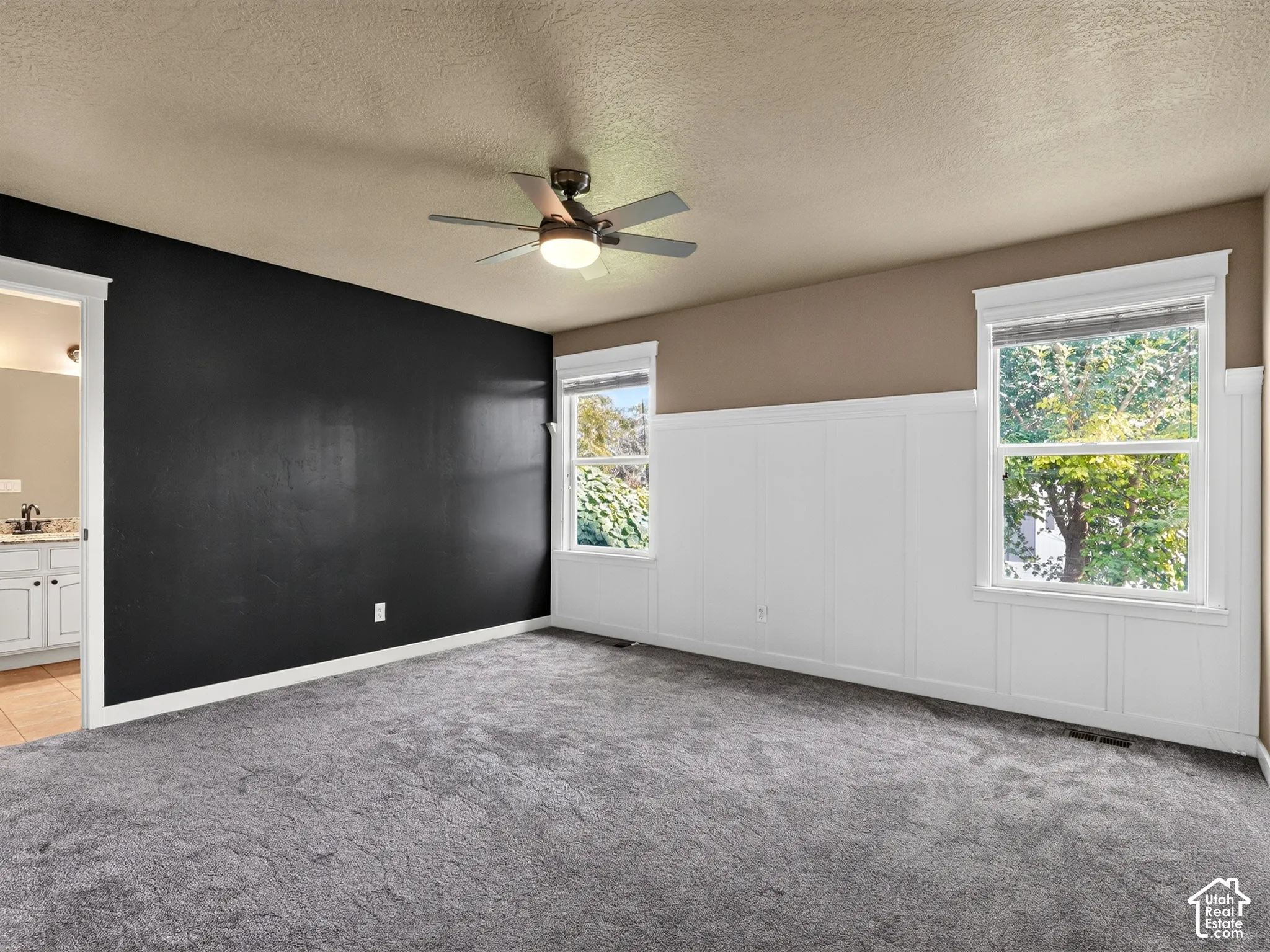 Plush gray carpeting, dual windows with white trim, white wainscoting, and a ceiling fan with integrated lighting
