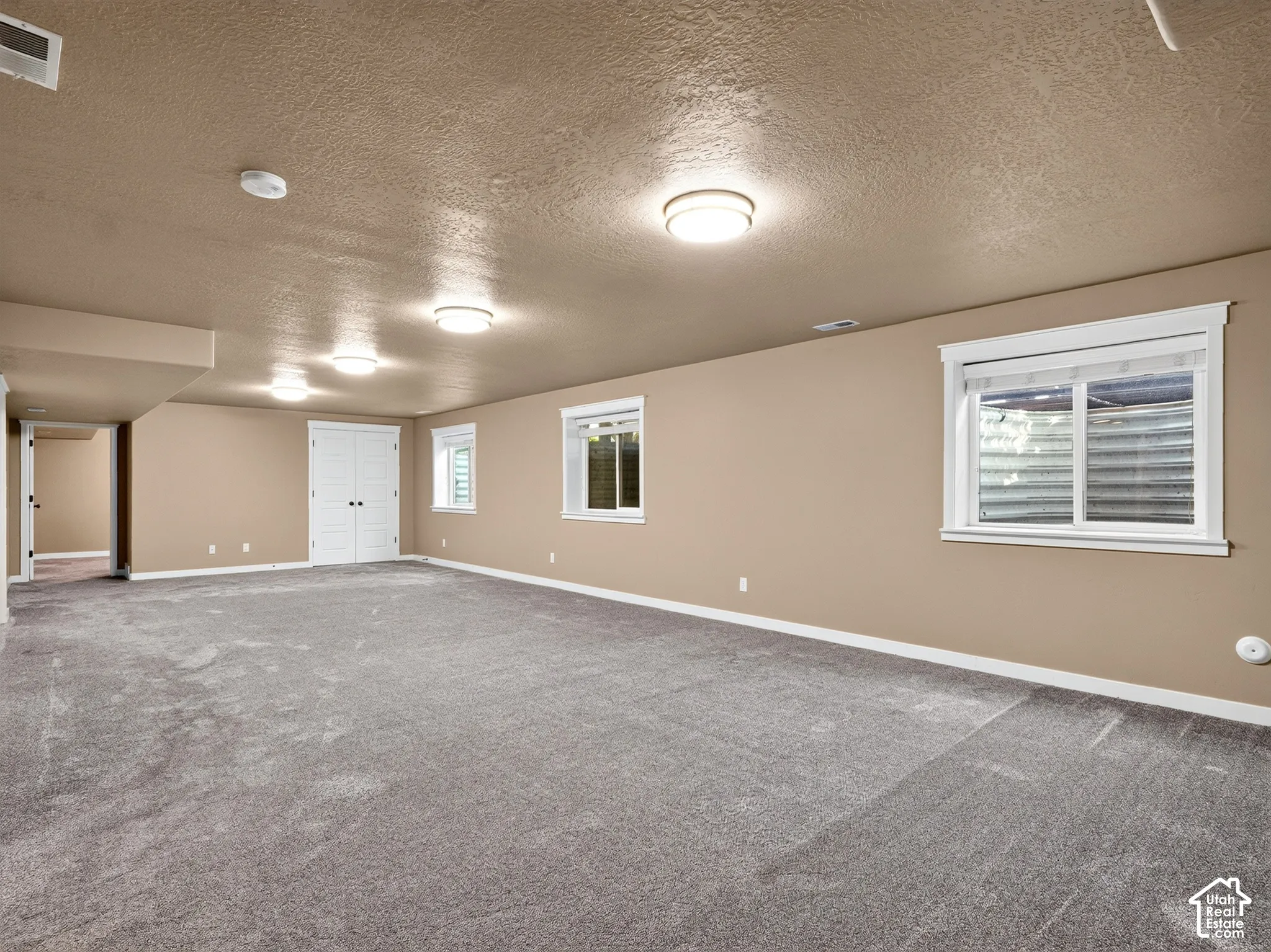 Spacious room featuring gray carpeting, multiple windows with white trim, double white paneled doors, and recessed lighting