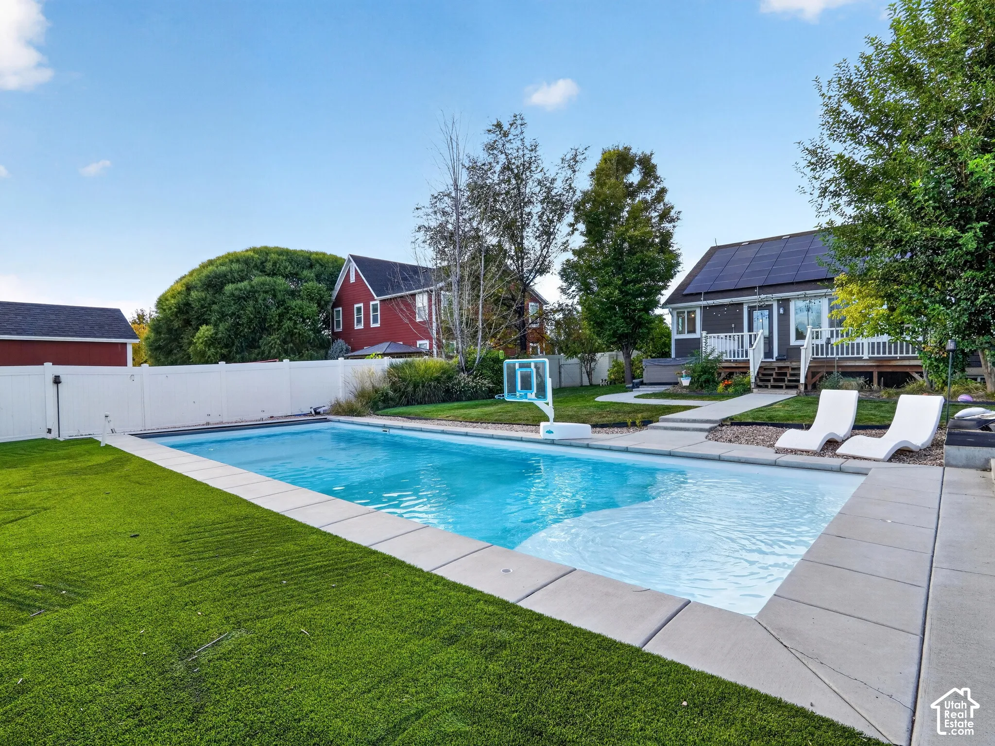 In-ground swimming pool with concrete surround, artificial turf, and a white privacy fence