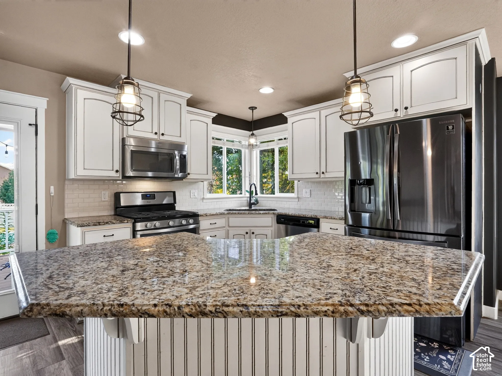 Kitchen featuring a large island with stone countertops, white shaker-style cabinetry, subway tile backsplash, and stainless steel appliances