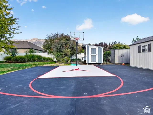 Hardscaped sports court with a basketball hoop, bordered by a white privacy fence and a manicured lawn