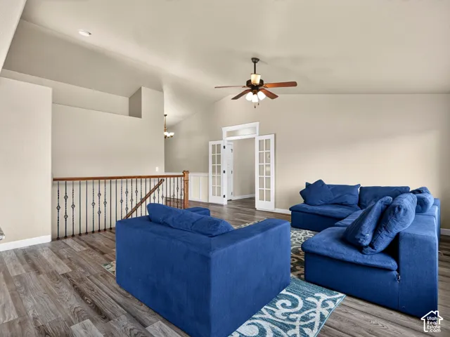 Vaulted ceilings, wood-finish flooring, white French doors, ceiling fan, and a staircase with a wood handrail and wrought iron balusters