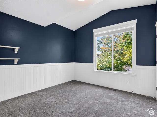 Vaulted ceiling with white paint, dark blue accent walls, wainscoting, and a large window