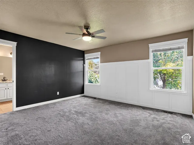 Plush gray carpeting, dual windows with white trim, white wainscoting, and a ceiling fan with integrated lighting