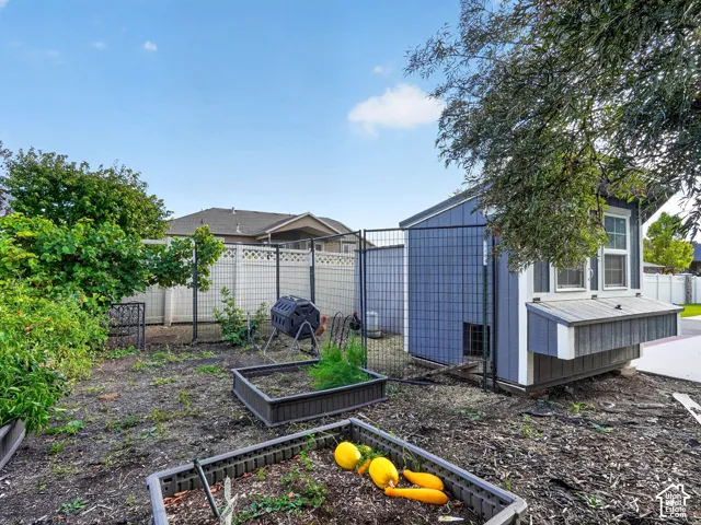 Detached outbuilding with multiple windows, fenced enclosure, and planting beds