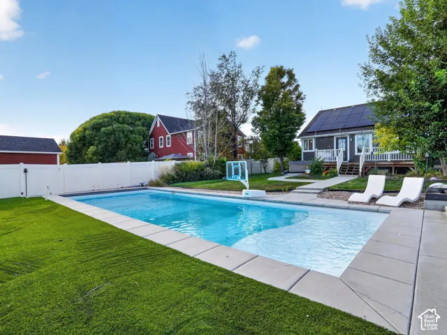 In-ground swimming pool with concrete surround, artificial turf, and a white privacy fence