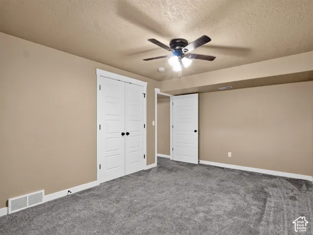 Spacious room featuring neutral tone walls, dark grey carpeting, a ceiling fan with integrated lighting, and white paneled doors with black hardware