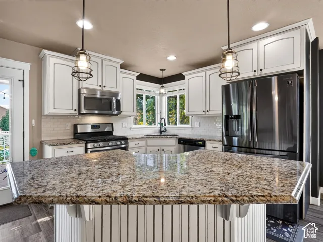 Kitchen featuring a large island with stone countertops, white shaker-style cabinetry, subway tile backsplash, and stainless steel appliances