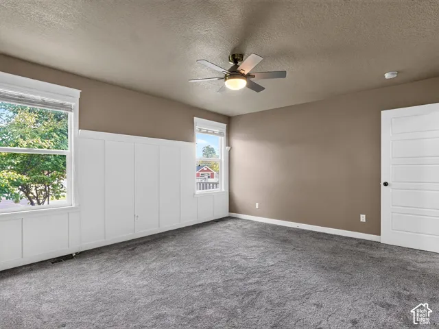 Neutral-toned walls with wainscoting, a ceiling fan with integrated lighting, and plush grey carpeting