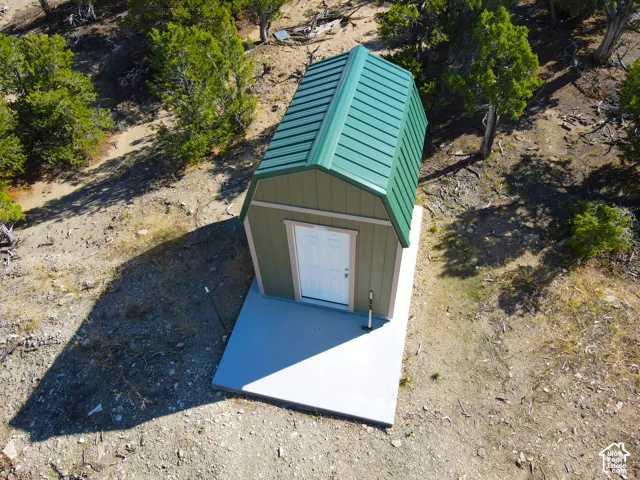 Green metal gambrel roof structure with a white entry door and a concrete pad