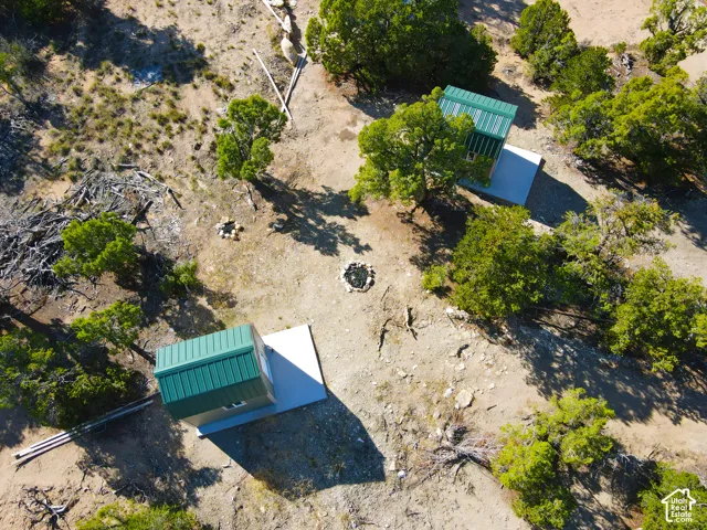 Two compact structures with green metal roofs, each on a concrete pad, surrounded by natural vegetation