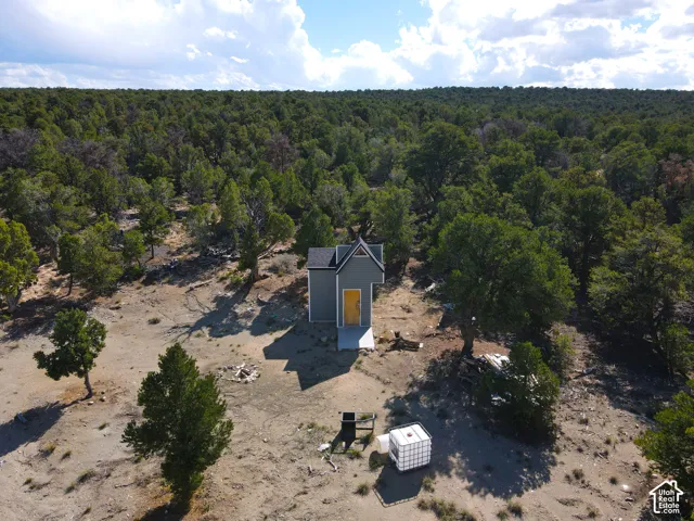 Detached structure with gray siding and a black roof, featuring a vibrant yellow door and a small concrete landing, surrounded by natural woodland