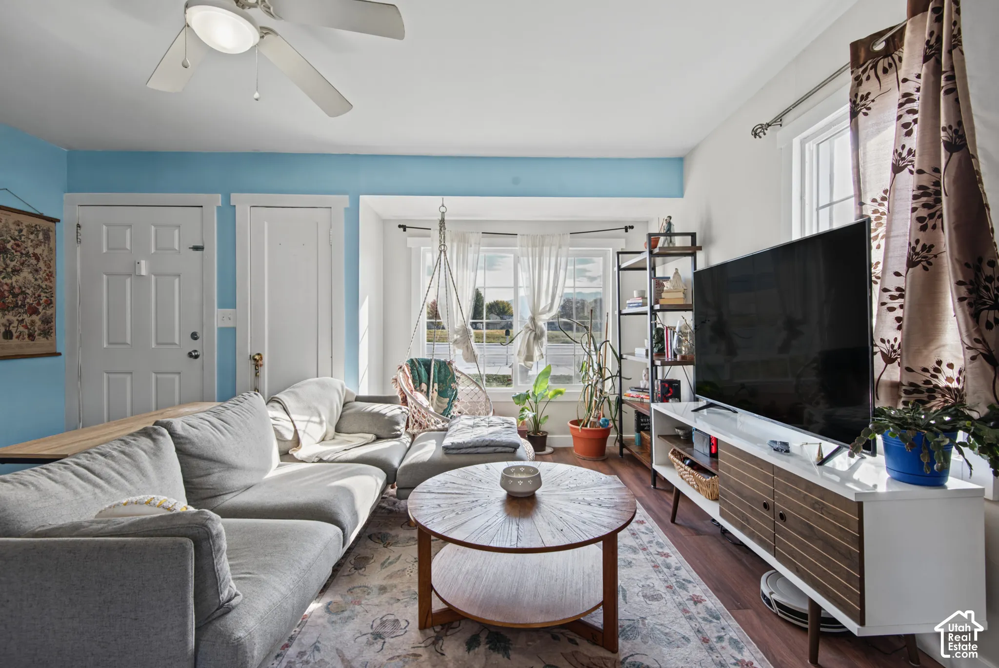Hardwood-style flooring, a ceiling fan, and multiple windows with natural light