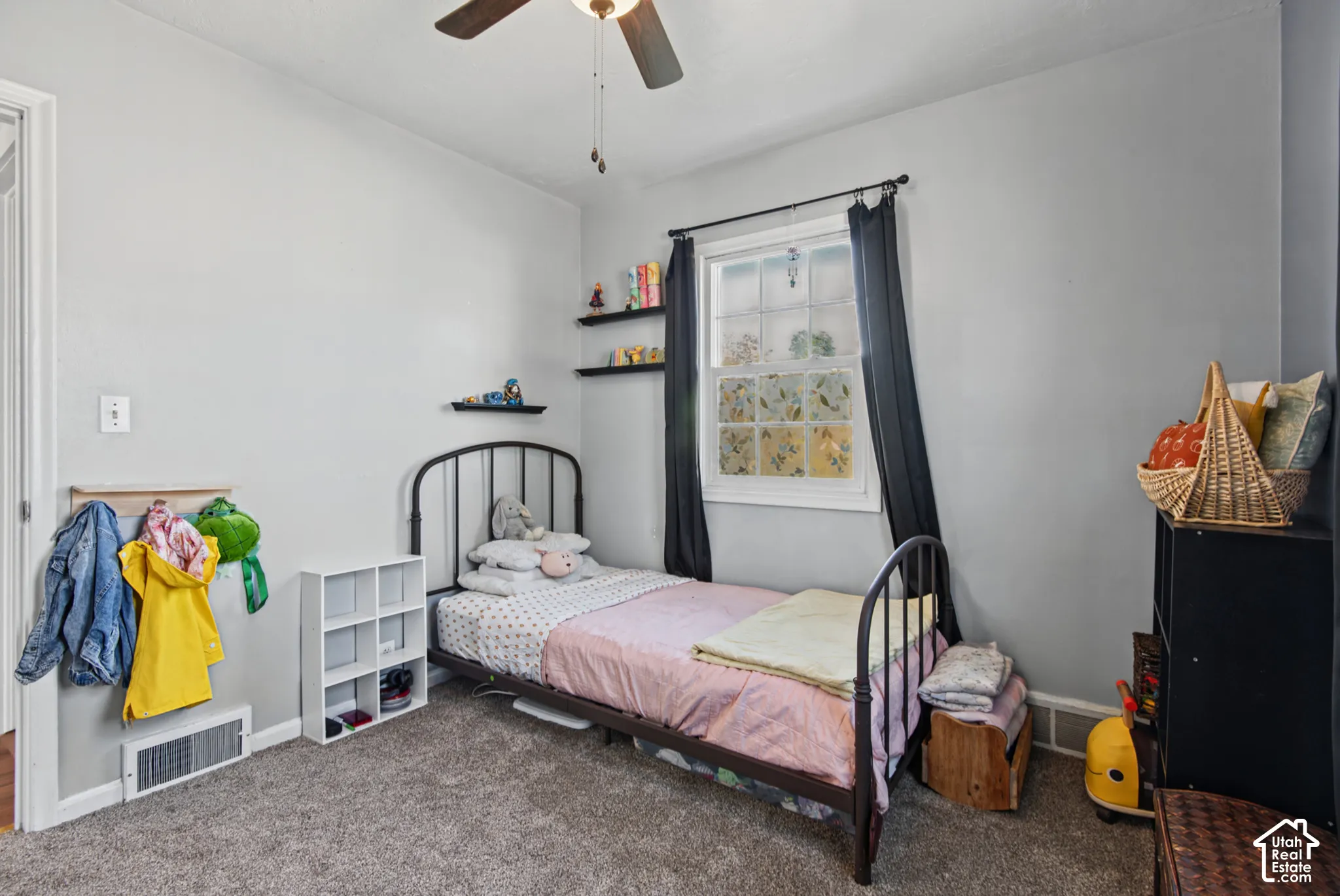 Carpeted room with a ceiling fan, a window with dark drapes, and built-in shelving units