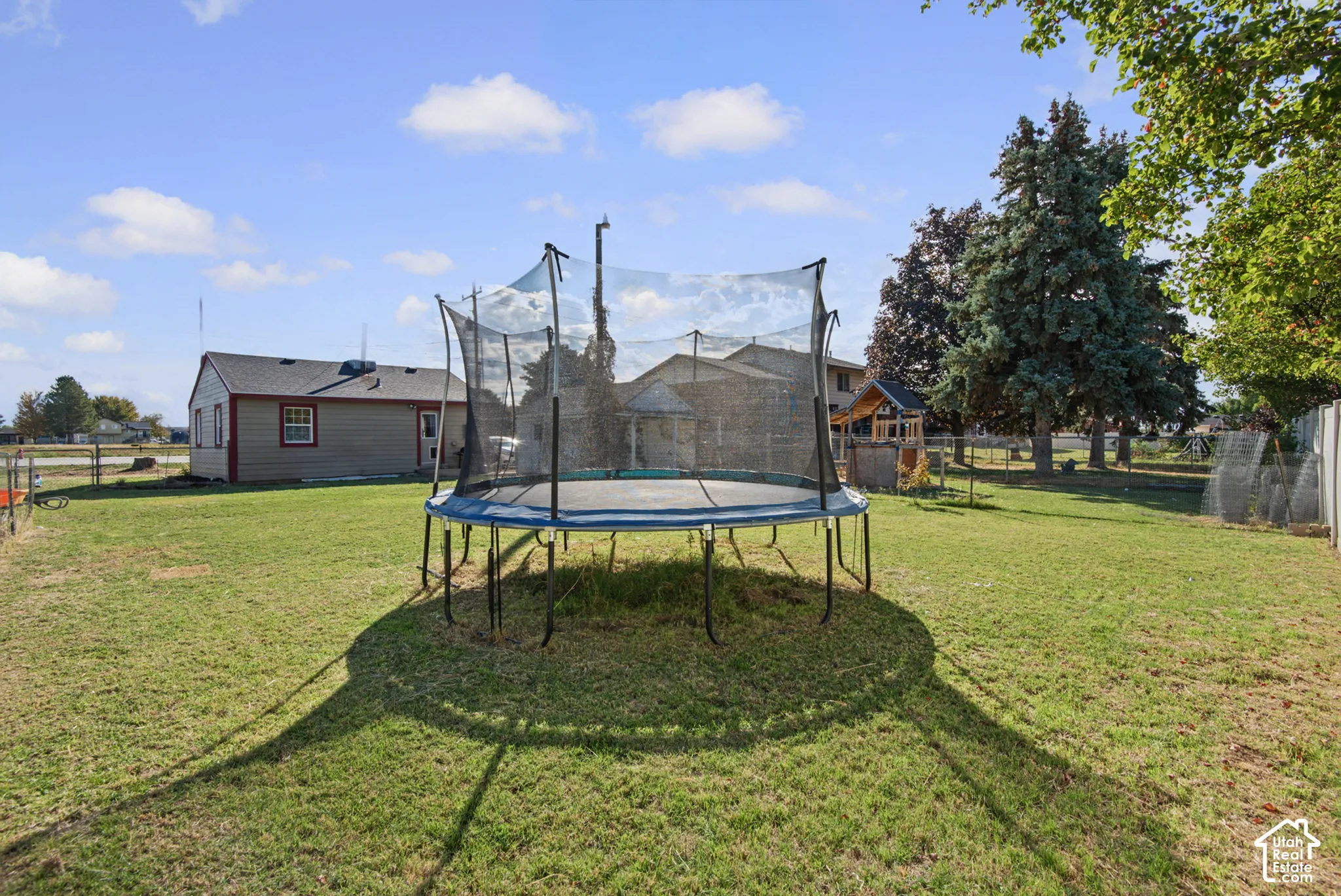 Expansive grassy yard with mature trees and a chain-link fence
