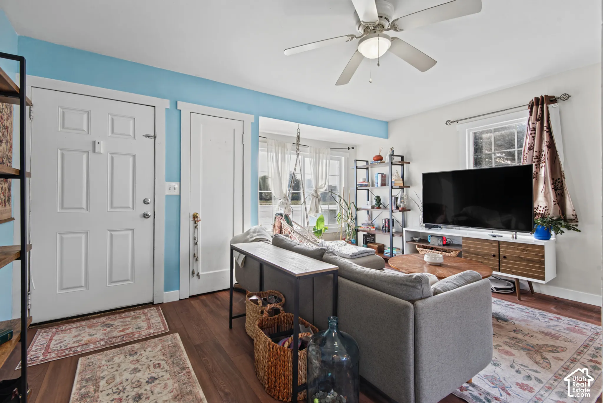 Wood-finish flooring throughout, featuring a ceiling fan with integrated lighting, and multiple windows allowing natural light