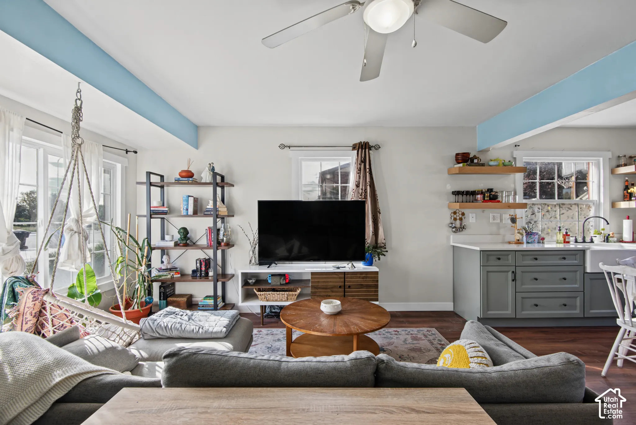 Living area featuring wood-finish flooring, a ceiling fan, and multiple windows providing natural light