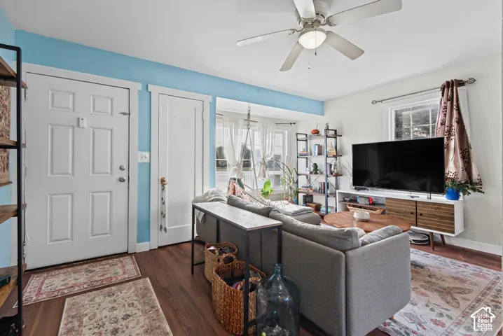 Wood-finish flooring throughout, featuring a ceiling fan with integrated lighting, and multiple windows allowing natural light