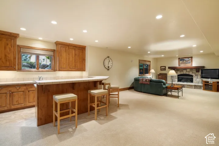 Spacious recreation area featuring a built-in wet bar with wood cabinetry, a stone-faced fireplace with a wood mantel, recessed lighting, and light-toned carpeting