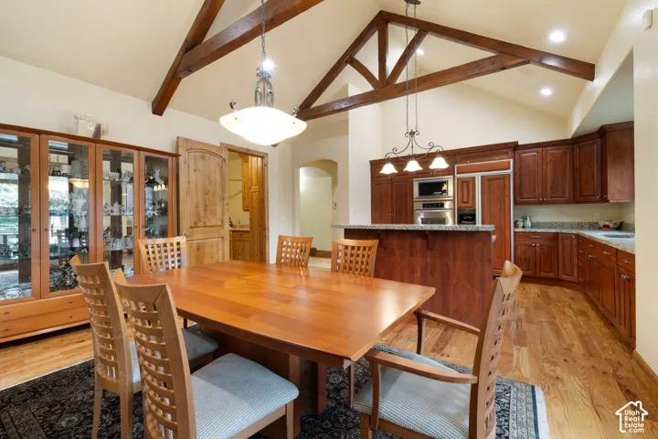 Vaulted ceilings with exposed wood beams, hardwood flooring, and a kitchen featuring built-in stainless steel appliances, wood cabinetry, and stone countertops