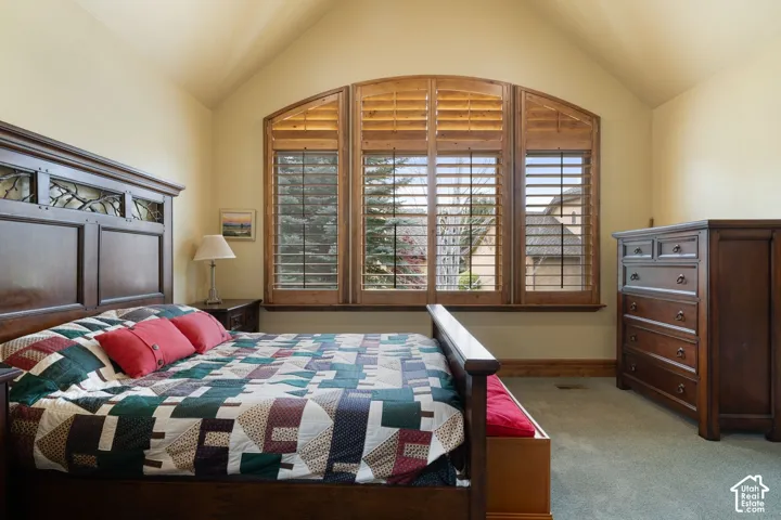Arched window with wood shutters, vaulted ceiling, and carpeted flooring
