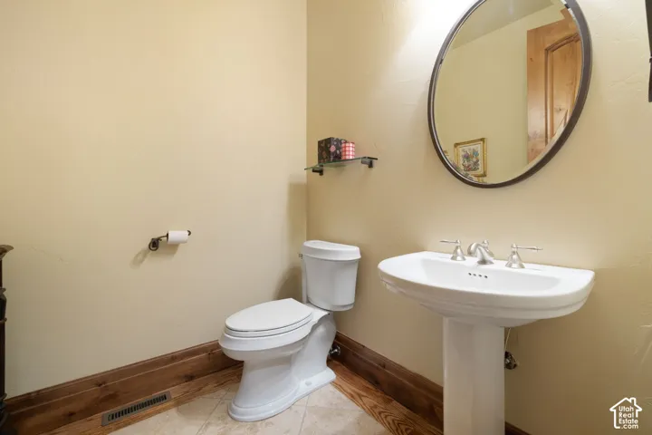 Pedestal sink with dual-handle faucet, oval mirror, and wood-finish baseboard trim