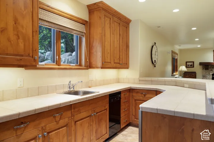 Wood cabinetry with under-cabinet lighting, stainless steel sink, tile countertops, and recessed ceiling lighting