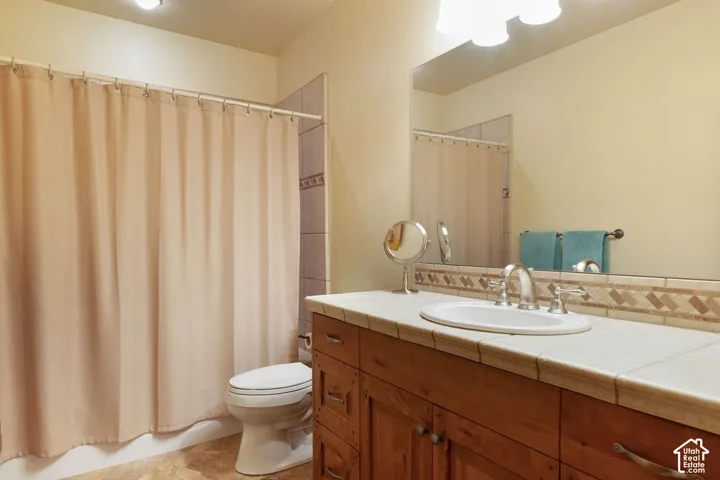 Bathroom featuring a wood-finish vanity with a tile countertop, a drop-in sink, and a framed mirror