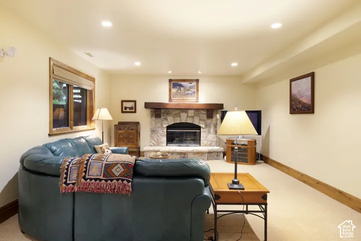 Stone fireplace with a wood mantel, recessed lighting, wood-trimmed window, and carpeted flooring