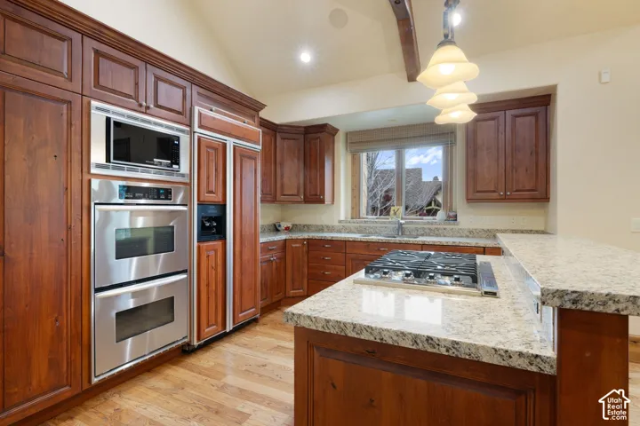 Wood-finish cabinetry with stainless steel appliances, granite countertops, a gas cooktop, and wood-finish flooring