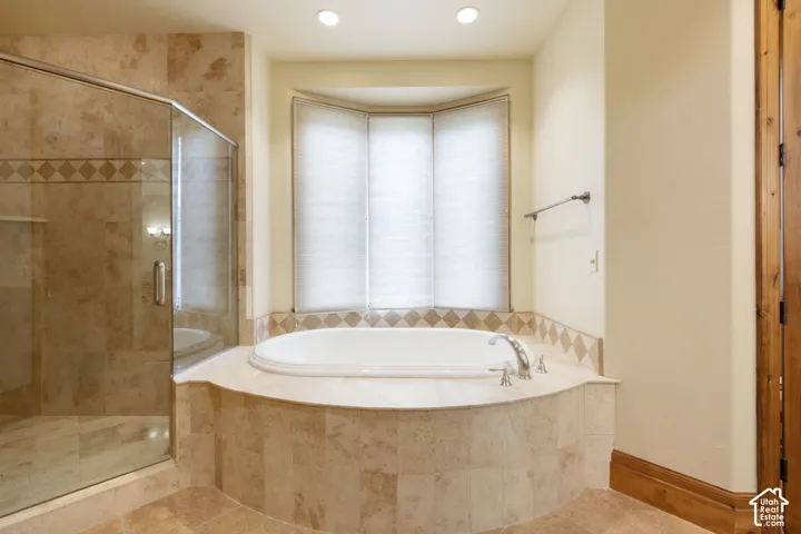 Recessed lighting illuminates the soaking tub and glass-enclosed shower, both featuring stone-finish tile surrounds with decorative banding