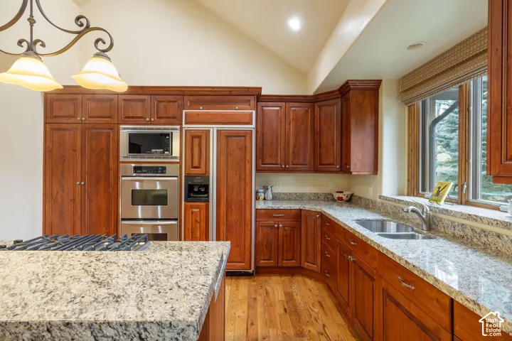 Custom cabinetry with integrated appliances, stainless steel double oven, stainless steel microwave, wood-finish flooring, and light-toned countertops