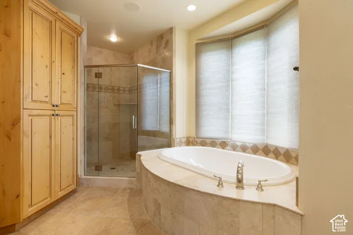 Built-in soaking tub with deck-mounted fixtures, enclosed shower with glass door, natural wood-finish cabinetry, and recessed lighting