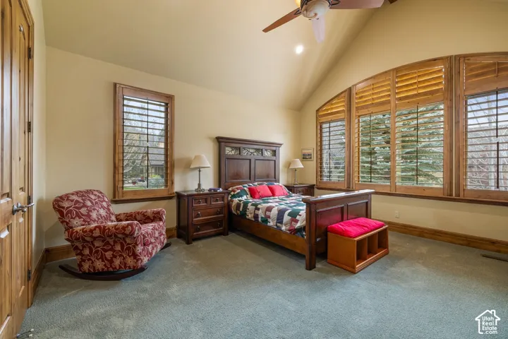 Vaulted ceiling with a ceiling fan, arched window, wood plantation shutters, wood-finish door, and wall-to-wall carpeting