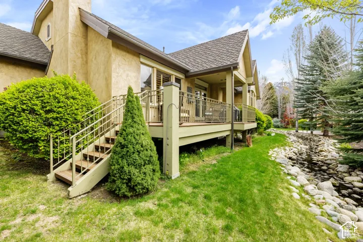 Exterior stucco siding, multi-level deck, metal deck railing, sloped lawn, and rock-lined water feature