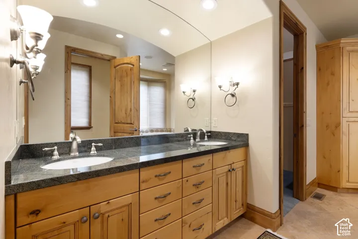 Dual vanity with undermount sinks, stone countertop, wood-finish cabinetry, and recessed lighting