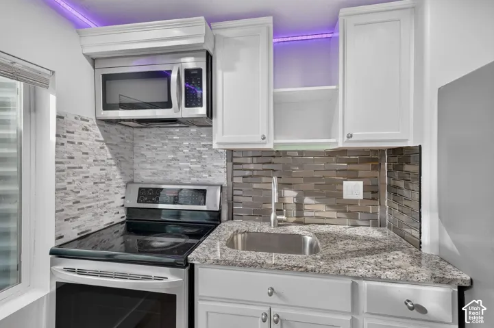 Stainless steel appliances, granite-style countertops, white cabinetry, undermount sink, and tiled backsplash