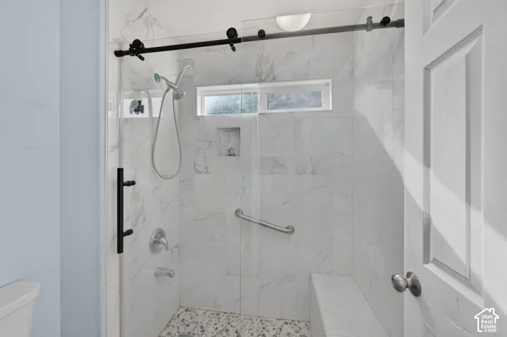 Shower enclosure featuring a sliding glass door with black hardware, marble-look tile walls, a built-in bench, a recessed niche, and a pebbled floor