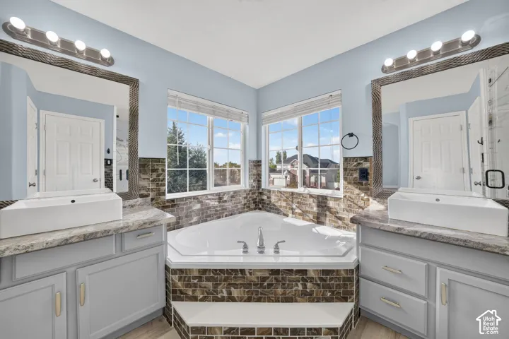 Corner soaking tub with tile surround, dual vessel sinks, and light-toned cabinetry