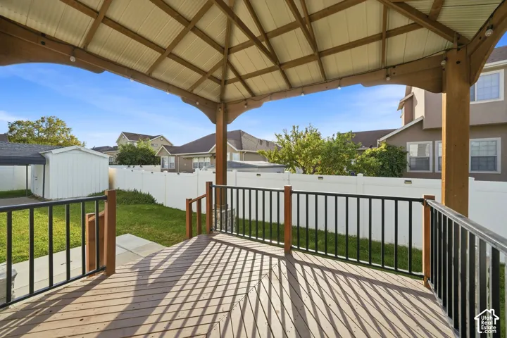 Covered wood-finish deck with black metal railings, leading to a fenced backyard with a shed