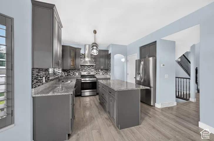 Kitchen featuring gray cabinetry, granite countertops, a mosaic tile backsplash, stainless steel appliances, and wood-finish flooring