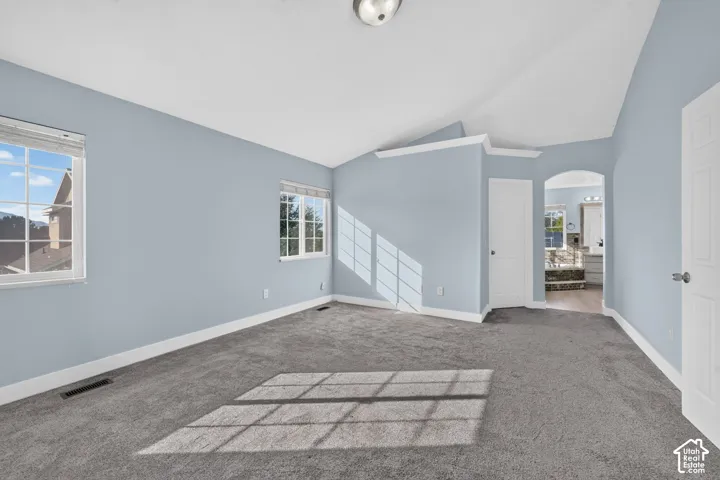 Vaulted ceiling, two windows with blinds, gray carpet, archway, and white trim