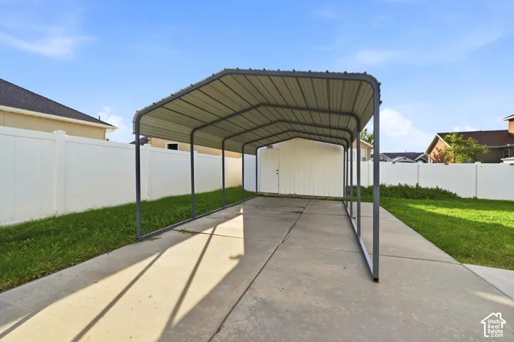 Covered parking structure over concrete driveway, complemented by a white privacy fence and a separate storage shed