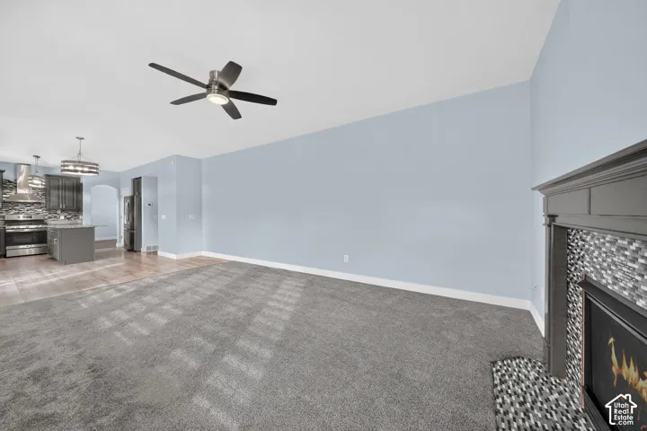 Fireplace with tile surround, stainless steel kitchen appliances, wood-finish flooring, built-in cabinetry, and a ceiling fan